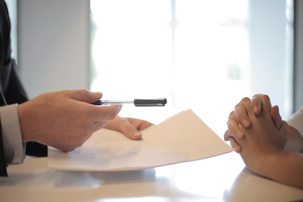 a hand handing a pen and a document to another person