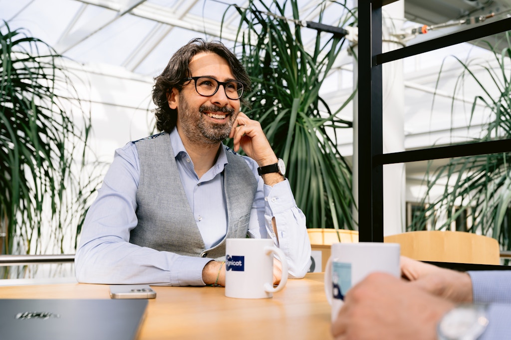 Smiling man sitting on a desk with his elbow on the table and